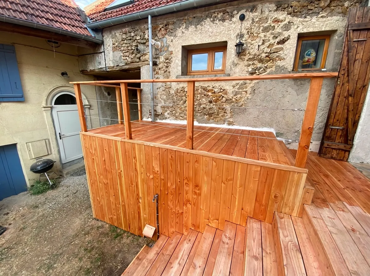 Platelage bois et garde-corps à câbles inox d'une terrasse surélevée devant une façade en pierre apparente, en Essonne (91)